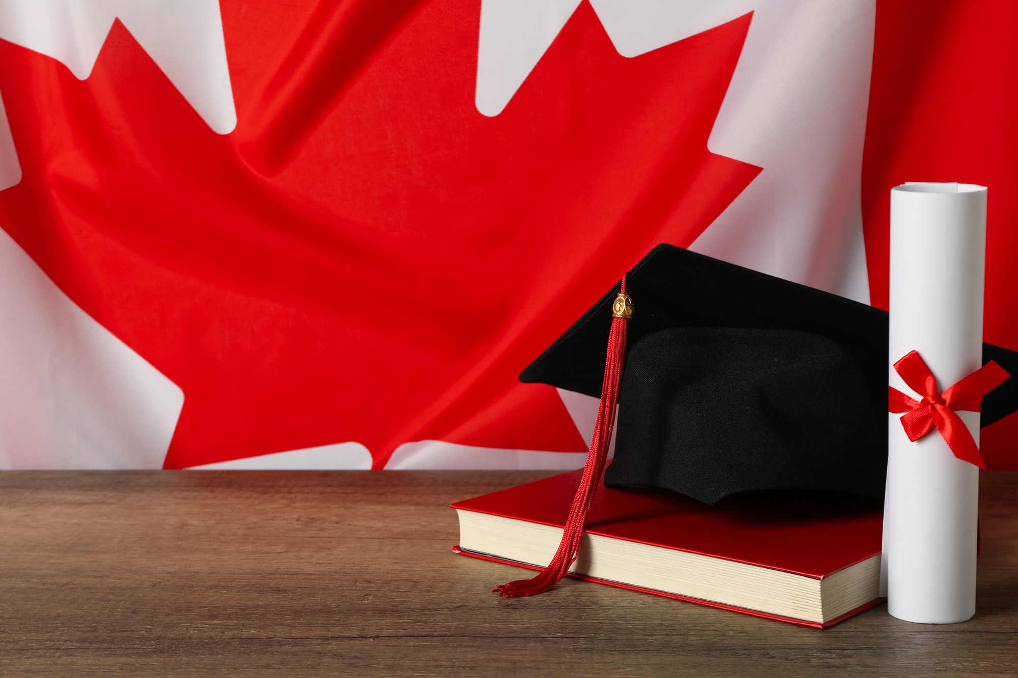 Graduation hat, book and diploma, on the background of the Canadian flag.